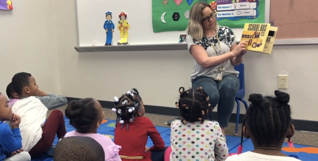 Teacher leading writing-focused read-aloud to preschool students on carpet